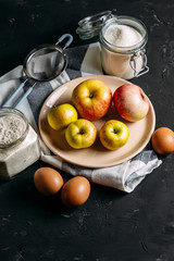 Autumn apple pie. Ingredients and cooking. Apples, eggs, flour, sugar. On a dark wooden background with copy space. Top view
