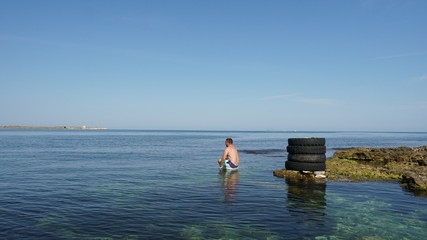 Fototapeta na wymiar Brave man jumping to the deep blue sea from old tires on the coast.
