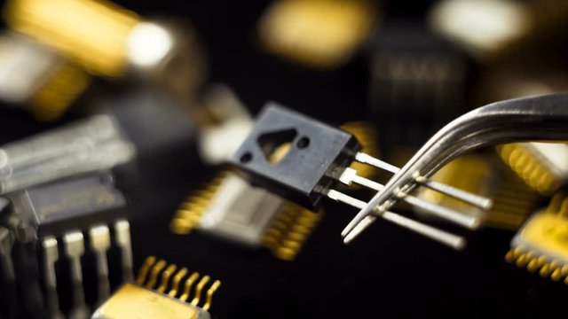 Transistor with tweezers on the background of electronic components.