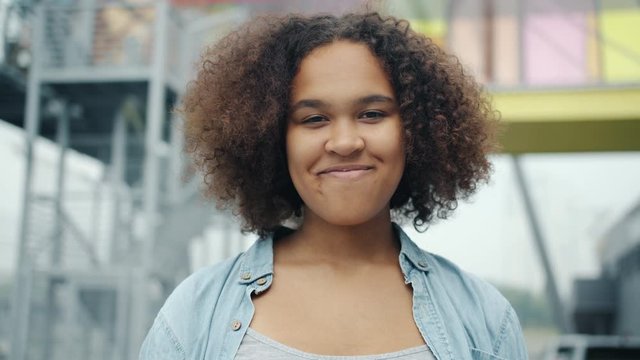 Close-up portrait of attractive African American teenager smiling standing outdoors looking at camera. Beautiful people, urban background and positive emotions concept.