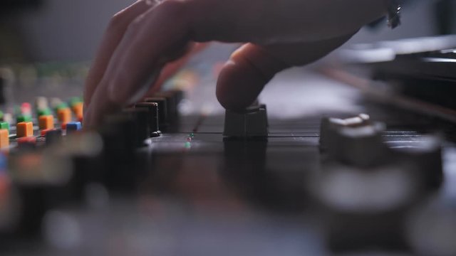 Side view of professional digital audio console in record studio. Close up fingers of music producer working on sound control panel of audio workstation with mixing console in sound recording studio