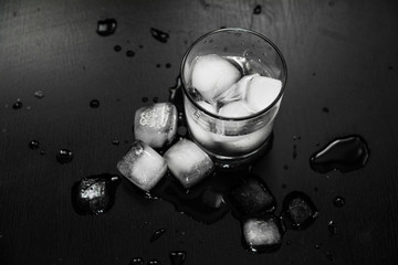 glass with ice on a black background. melting ice around splashing drops