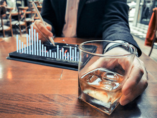 business man with beard who has smart watch using pro tablet and pencil interacting with tablet screen holographic economy floating graphics data drinking whiskey in the cafe pub