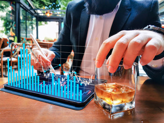 business man with beard who has smart watch using pro tablet and pencil interacting with tablet screen holographic economy floating graphics data drinking whiskey in the cafe pub
