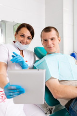 Fototapeta premium Happy dentist and patient commenting treatments in a tablet application in a consultation with medical equipment in the background