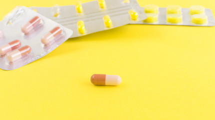 One tablet close-up against other capsules on a yellow background.The concept of medicine.Medicines for the treatment of diseases, viruses, autumn cold, beriberi, hypothermia, vaccination.