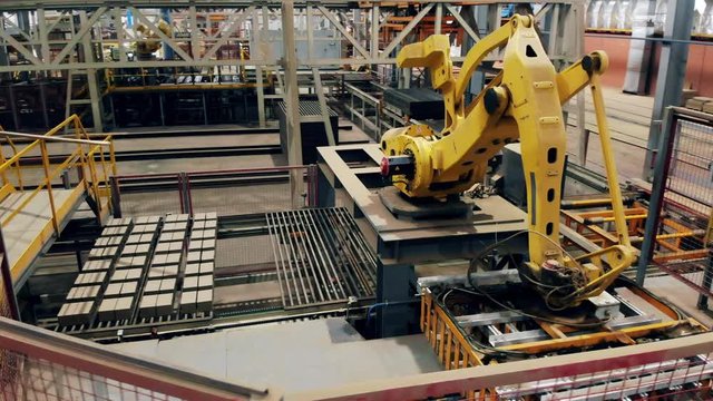 Robotic arm at factory floor sorts bricks on a conveyor.