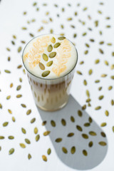 Milky latte with pumpkin seeds on froth, served on white background with spreaded pumpkin seeds