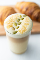 Milky latte with pumpkin seeds on froth, served on white background with french crunchy croissants
