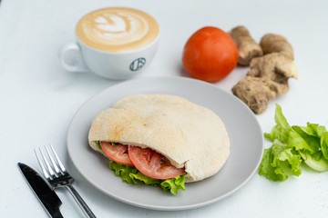 A cup of nice cappuccino and pita, stuffed with veggies and chicken breast on a white table in cafe