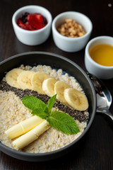 Close up of whole grain porridge with different toppings, served on dark table as a healthy substantial breakfast