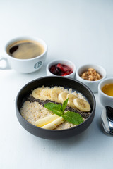 Healthy sweet breakfast with whole grain porridge, chia seeds, butter, banana and other toppings, served with a cup of black coffee on a white background
