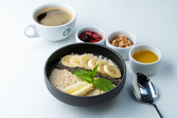 Healthy sweet breakfast with whole grain porridge, chia seeds, butter, banana and other toppings, served with a cup of black coffee on a white background