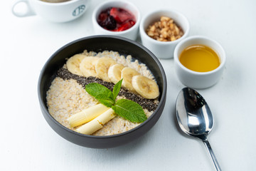 Healthy sweet breakfast with whole grain porridge, chia seeds, butter, banana and other toppings, served with a cup of black coffee on a white background