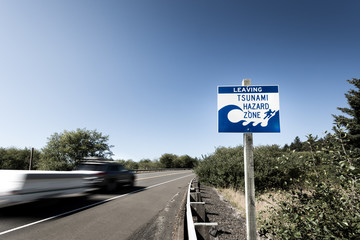 A tsunami warning sign along a coastal highway with a blurred car passing by near the Oregon coast.