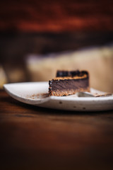 Slice of raw vegan rich dark chocolate cake on a white plate at restaurant. Closeup, minimalism food photograohy concept