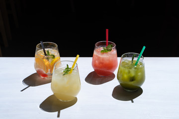 Side view of various of refreshing summer lemonades: classic lemon soda, strawberry lemonade, ginger spicy lemonade and estragon soda served on a white background