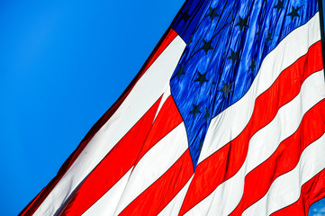 Backlit American flag waving in the wind against a perfect blue sky
