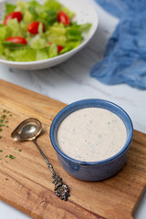 Homemade Buttermilk Ranch Dressing in Blue Bowl on White Countertop; Prepared Salad in Background