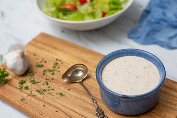 Homemade Buttermilk Ranch Dressing in Blue Bowl on White Countertop; Prepared Salad in Background