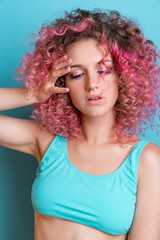 Naklejka premium Portrait of beautiful woman with pink curly colored hairs in blue swimsuit. Glitter makeup. 90s style. Ombre. Isolated on blue