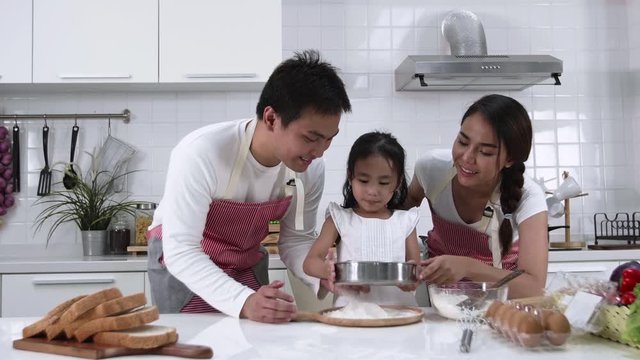 Happy Asian family Father, Mother and Daughter are sieving flour preparing the dough, bake cookies in the kitchen. family cooking food Concept.