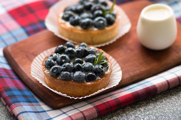 Tartlets with blueberries on the wooden board with a checkered napkin. Top view