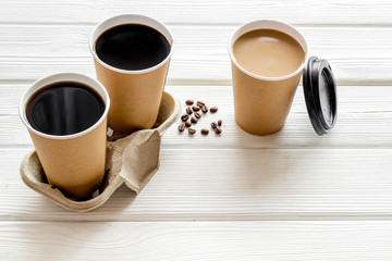 Coffee to take away in paper cups with lids and beans on white wooden table background