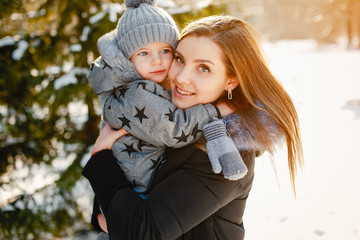 Mother with cute son in a winter park. Little boy in a gray overalls