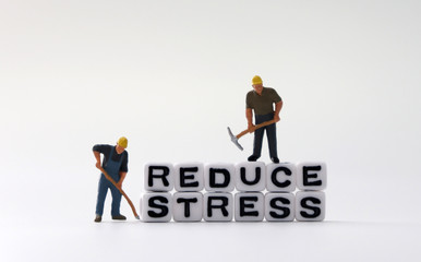 The word STRESS and the word REDUCE on white cubes with miniature people.