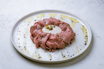 vitello tonato on a plate on white concrete table