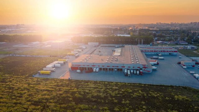 Aerial hyper lapse (motion time lapse) of the large logistics park with warehouse, loading hub with many semi-trailers trucks standing at the ramps for load/unload goods at sunset