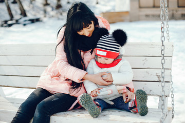 Family in a winter park. Elegant woman in a pink jacket. Mother with little daughter sitting on the bench