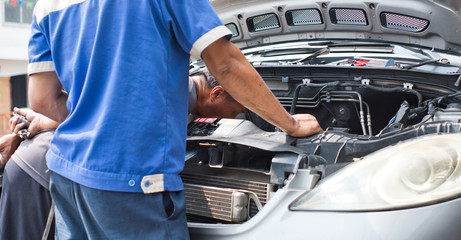 Back view of real people car mechanic fixing or repairing the engine stand in front of car open...