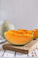 Fresh of sliced orange melon or cantaloupe on wooden cutting board on rustic white wood background.