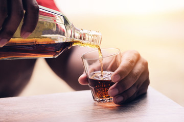 Pouring whiskey or alcohol drink from bottle to glasses on wooden  background - Pour liquor