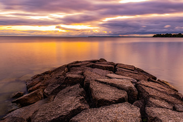 sunrise at Franklin Beach Conservation Area Ontario Canada with great view of the lake, clouds, light, pipe, trees, and stones.