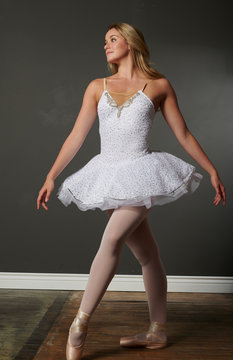 Beautiful and stunning blonde female ballerina dances in studio - white tutu, single dramatic spotlight