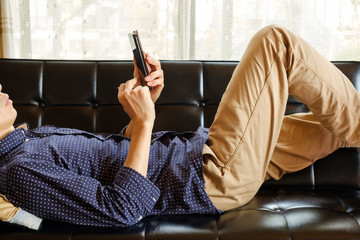 自宅のソファでスマートフォンを操作する男性 ネットサーフィン SNS 暇つぶし