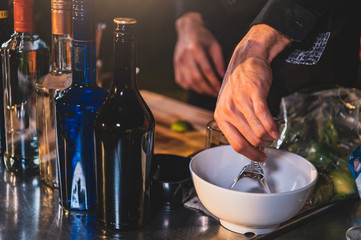 Closeup of alcoholic bottles with bartender hand preparing fresh lime lemonade cocktail in drinking wine glass with ice at night bar clubbing counter. Occupation and people lifestyles concept