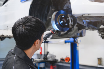 Asian male mechanical hold and shining flashlight to examine car disk brake pad wear of automotive vehicle. Safety suspension inspection check service maintenance for customer before road trip concept