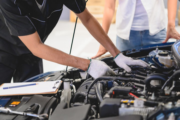 Fototapeta na wymiar Asian male auto mechanic examine car engine breakdown problem in front of automotive vehicle car hood with female customer. Safety technical inspection care check service maintenance for road trip