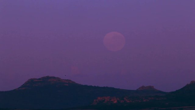Timelapse of Red full moon setting over a mountain, in a purple night sky.