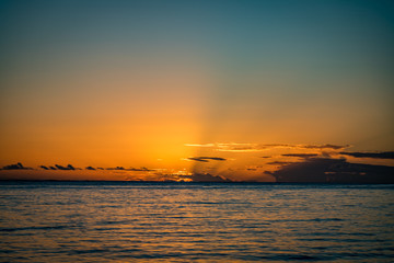 Low clouds block a small bit of sun as it passes below the horizon on a calm ocean at Anaeho'omalu Beach on the Big Island of Hawaii