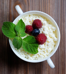 Cottage cheese with raspberries and blueberries in a bowl for healthy breakfast with ripe berries over rustic wooden background. Top view.