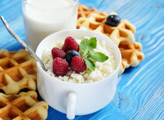 Time for breakfast. Cottage cheese with berries, waffles and milk on a wooden blue background.