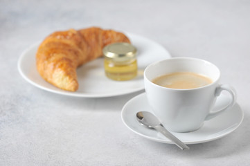 Coffee with croissant on a light background. Near the croissant a jar of honey. Close-up. Free space for text.
