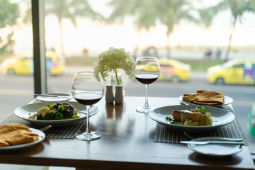 Fresh romantic breakfast table next to morning briliant light window, with beef, salmon fish, mashed potato, vegetable, red wine