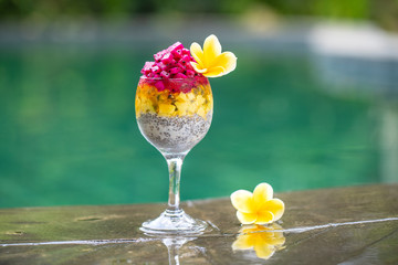 Chia seeds pudding with red dragon fruit, passion fruit, mango and avocado in a glass for breakfast on the background of the swimming pool water, closeup. The concept of healthy eating.
