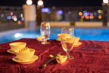 Empty glasses on table prepared for dinner next to swimming pool at night.